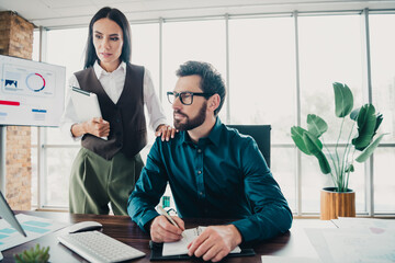 Business colleagues collaborate in a modern office as one writes notes and the other reviews charts...