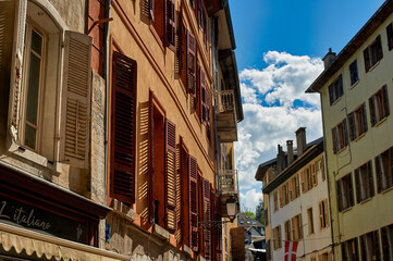 Fototapeta premium Charming old town street in Haute-Savoie, France. Traditional buildings with warm orange facades and classic wooden shutters under a bright blue sky.