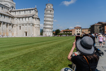 Woman photographing leaning tower and cathedral on green square.