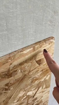Oriented chipboard close-up. A woman's hand touches a osb wooden board made of sawdust. Building material for roughing