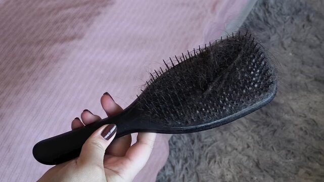 Dark hair falling out on a hair comb in a woman's hand close-up. Hair loss