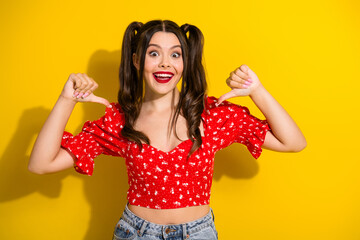 Glamorous young woman with ponytails in a red floral top stands happily yellow background casual...