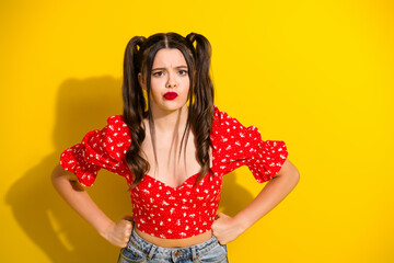 Young glamorous girl in red floral top posing with hands on hips against yellow background