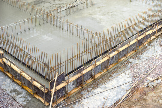 Monolithic foundation casting, fresh concrete poured into formwork with vertical rebar for structural walls. Base slab formation, reinforced concrete construction.