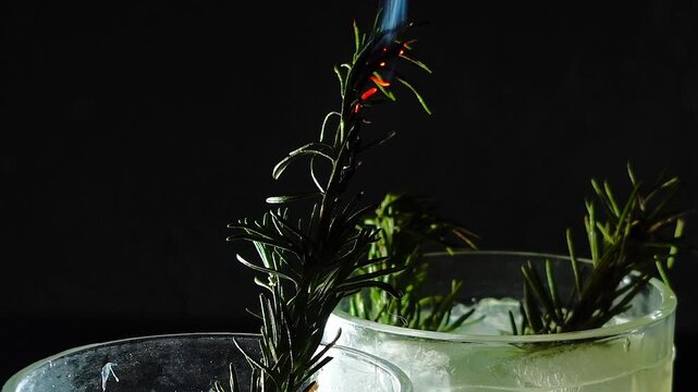 Delicious alcoholic cocktail made with jin tonic and ice in glasses for relaxing at night and refreshing in the summer. Spices and green lime for flavor. Bartender and bar. Rosemary burns with fire