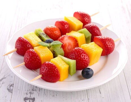 Vibrant fruit skewers (strawberry, kiwi, mango, blueberry) on white plate over light wood