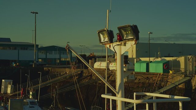 Close-up of ship mast with LED floodlights at harbor with golden sunrise and cyan sky, 4K.