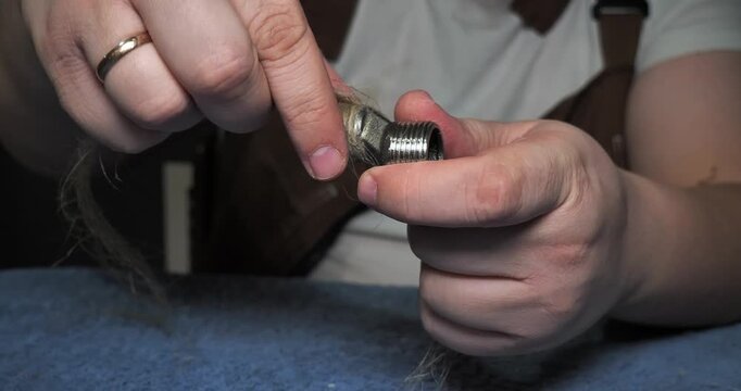 Professional plumbers wrap a metal fitting with flax tow to seal the threads. A plumber prepares pipes for installation and prevents leaks in the plumbing system. A plumber at work.