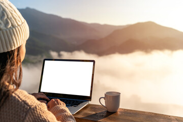 Young woman working with laptop and a cup of coffee with mountain view at sunrise in the morning,...