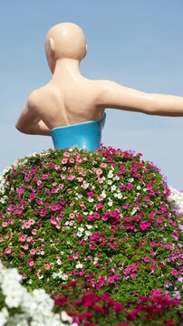 A beautiful spinning statue of a female dancer wearing a large, colorful skirt made entirely of blooming flowers. Creative floral landscaping and topiary art in a public garden
