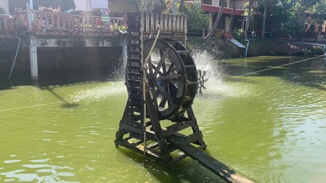 Traditional Wooden Water Wheel Spinning in Rural Thai Pond Under Sunlight