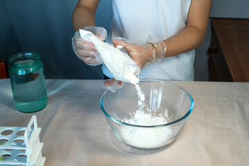 Close-up of gloved hands pouring a white substance into a glass bowl.