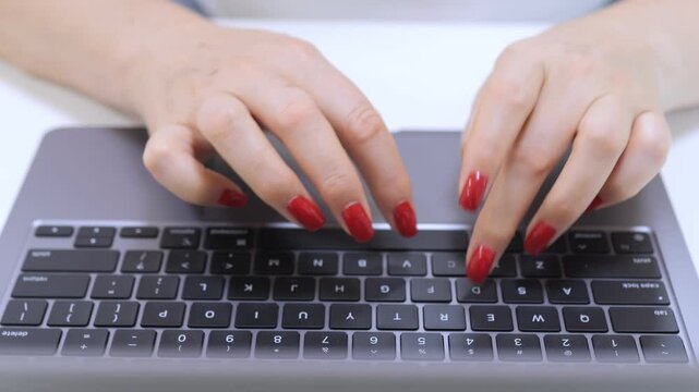 Woman is typing on a laptop keyboard. She has red fingernails. The keyboard has a number pad and a space bar