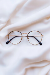 Stylish Round Gold-Rimmed Glasses Resting on Soft Draped Fabric