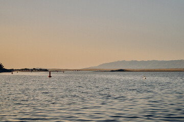 Calm sea with wooden pier and distant mountains at sunset, Croatia