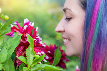 Fototapeta premium Smiling woman with colorful hair enjoys flowers in sunny garden
