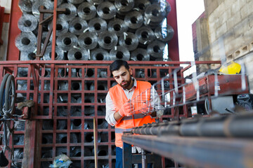 Worker fabricating steel rebar cage working at industrial construction supply facility with wire rolls