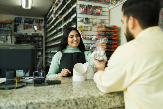 Woman sales clerk assisting customer at hardware store counter, holding plumbing fittings for service, retail shop experience