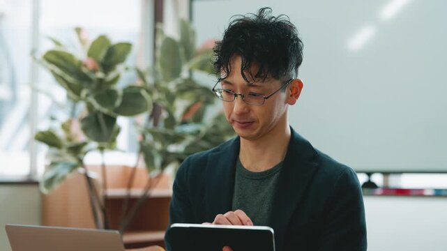 ノートパソコンとタブレットを使って作業する日本人ビジネスマンのオフィスシーン, Japanese businessman working with a laptop and tablet in the office