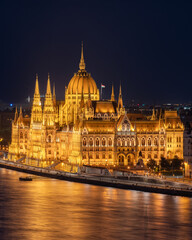 Fototapeta premium Blue hour view of the Hungarian Parliament illuminated along the Danube River. A majestic European cityscape showcasing Budapest iconic architecture at twilight
