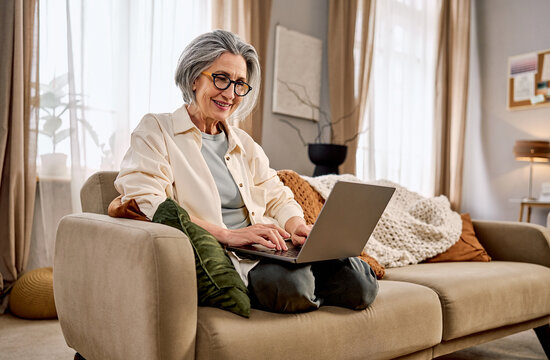 Smiling senior woman working on laptop from home in a cozy living room.
