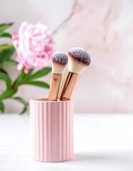 Makeup brushes stand in a pink ribbed holder. A peony bloom rests in the background with a marbled effect wall