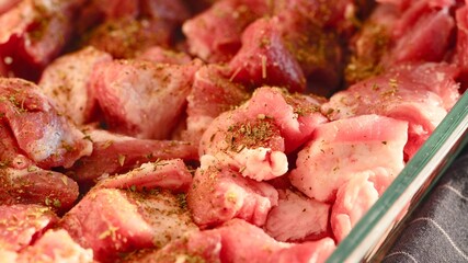 Close-up shot of pieces of raw pork meat with spice in a glass baking tray ready for cook.