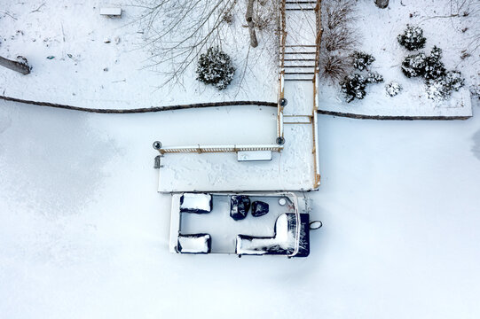 A pontoon boat sits frozen in a lake while tied to its dock until the lake melts in spring before it can be used.