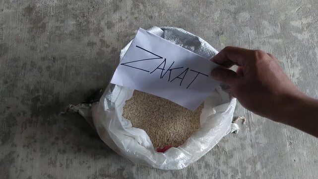 A hand holding a zakat note above a sack of rice. Concept of Islamic charity, food donation, Ramadan support, and helping people in need.
