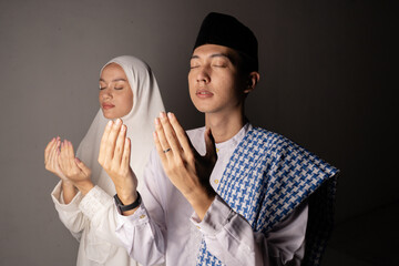 Man and woman praying together, studio portrait showing hands raised, headscarf, beads and patterned shawl creating serene