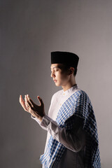 Young man praying in profile, dramatic side lighting emphasizes hands and shawl, calm contemplative mood with strong shadow