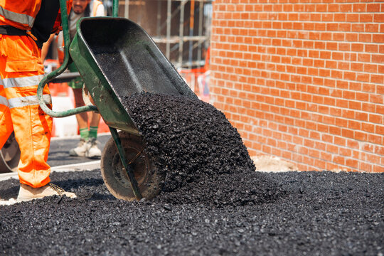 Workers pour asphalt from a wheelbarrow for road construction in a city