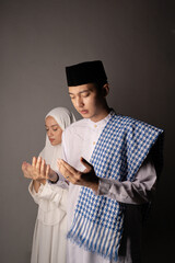 Man standing with companion praying behind, studio scene capturing supportive posture, raised hands, soft neutral backdrop, calm