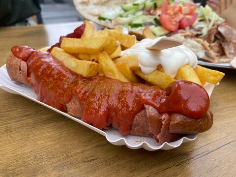 Berliner Currywurst mit Ketchup und Wellenschnitt-Pommes auf Pappteller. Klassisches deutsches Street-Food, frisch serviert. Ideal f&uuml;r Imbiss, Gastronomie, Essen und Alltag.
