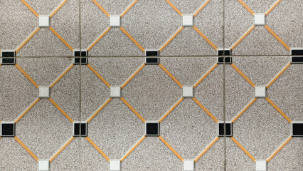 Horizontal front view of a ceramic tile pattern featuring grey textured diamond shapes with white and black square accents and orange diagonal lines.