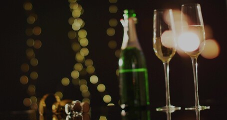Shimmering tall champagne flutes reflecting warm string lights at dim venue, with green bottle