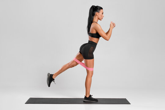 Fitness woman doing exercise for glutes with resistance band on gray background. Athletic girl working out