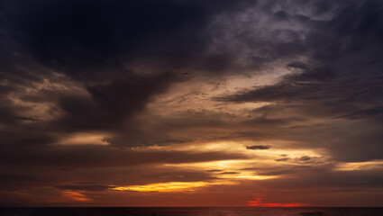 Fototapeta premium Sunset sky with dramatic clouds over sea water.Summer tropical beach view with colourfull orange,yellow,red,purple dark blue sky background for Travel concept