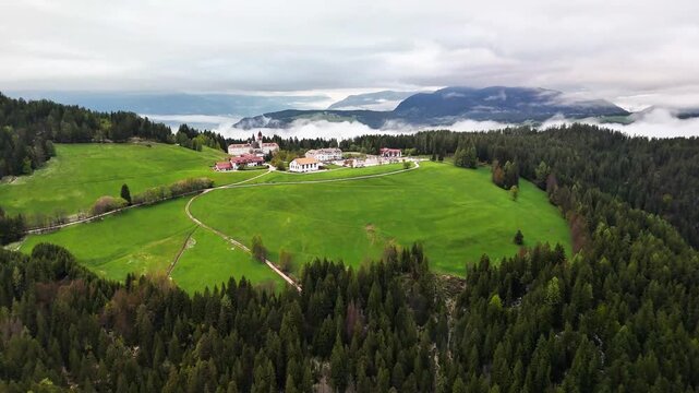 4K aerial of a hilltop village and monastery in South Tyrol, Italy&mdash;green meadows, conifer forest and rolling hills under low clouds with mountains beyond. Calm alpine scene, shot from drone.05.05.2025