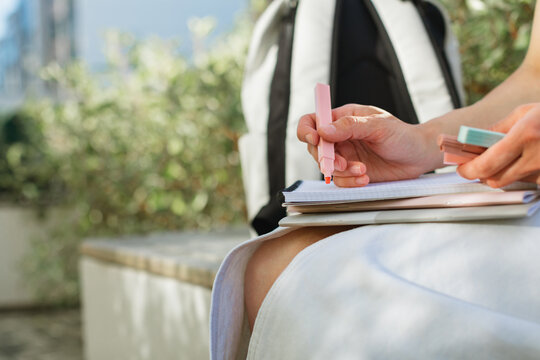 Close-up of a mid adult woman sitting on a park bench with a notebook and marker pens in her hands.