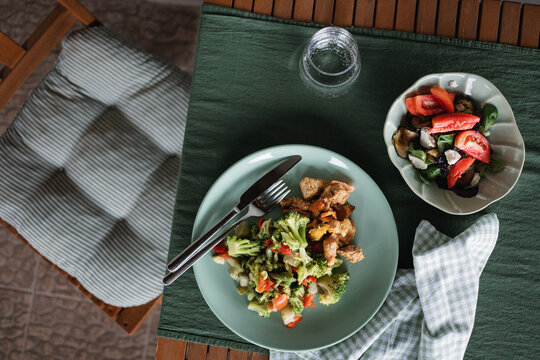 Overhead view of  grilled turkey with steamed vegetables, eggplant feta salad and a glass of water on a sunny terrace