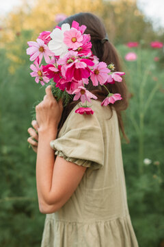 Side view of a young Woman standing in a garden holding a bunch of fresh pink cosmos flowers in front of her face