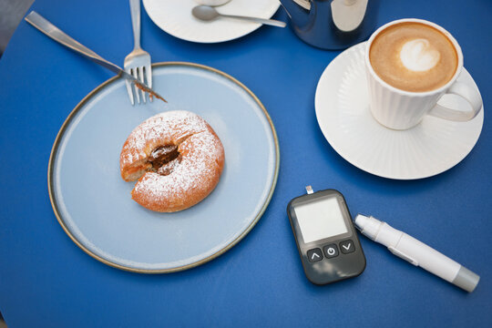 Overhead view of a doughnut and cappuccino on a table with a glaucometer