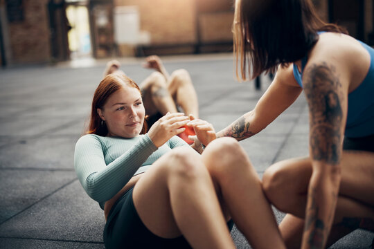 Smiling woman getting encouragement from her partner during a workout. She is wearing a blue top and has tattoos on her arms.