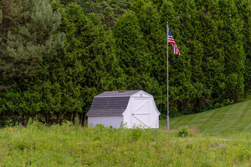White Storage Shed With American Flag Nestled Among The Trees In Summer In Wisconsin