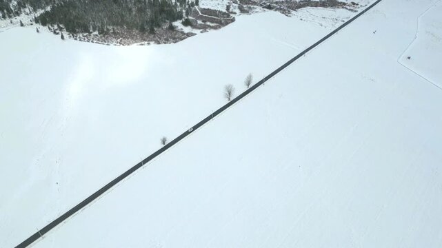 Drone aerial view of a car driving along a snow-covered rural road in West Virginia during winter