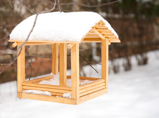 Wooden bird feeder covered with snow in winter garden. Cozy seasonal scene with natural light. Selective focus.