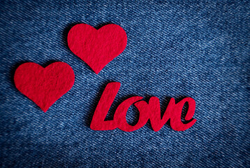 Romantic composition symbolizing warmth and tender feelings on Valentine's Day . Red felt word love with two hearts on blue denim fabric. Top view. Flatlay.