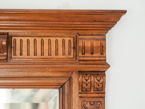 D&eacute;tail de moulures sculpt&eacute;s sur le cadre sup&eacute;rieur d'un miroir ancien en bois massif, au style n&eacute;oclassique