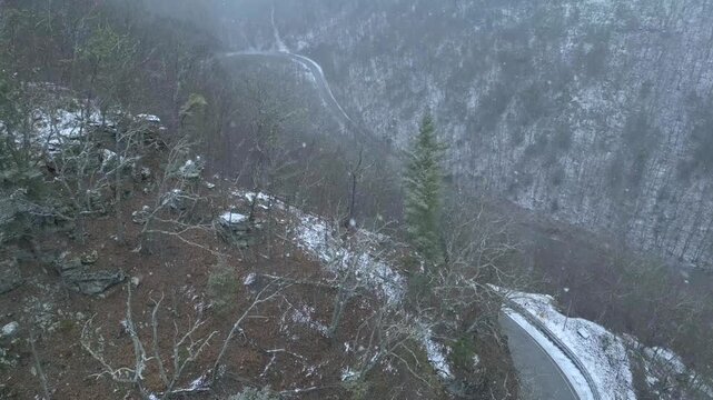 Drone aerial view of a snow-covered mountain with a winding road barely visible through heavy winter snowfall